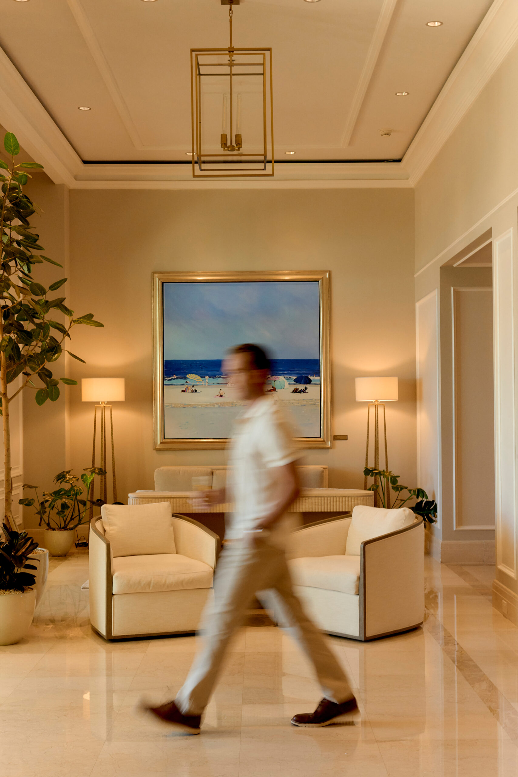 Man walking through elegant hotel lobby with cream seating and beach artwork on wall