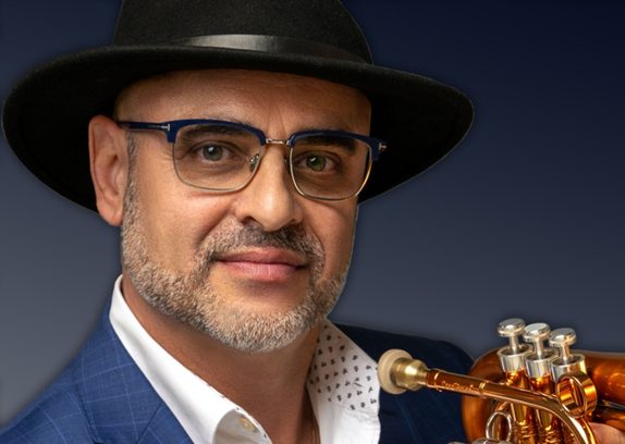 Bill Colletti holding a flugelhorn while posing in a blue checkered suit and hat.