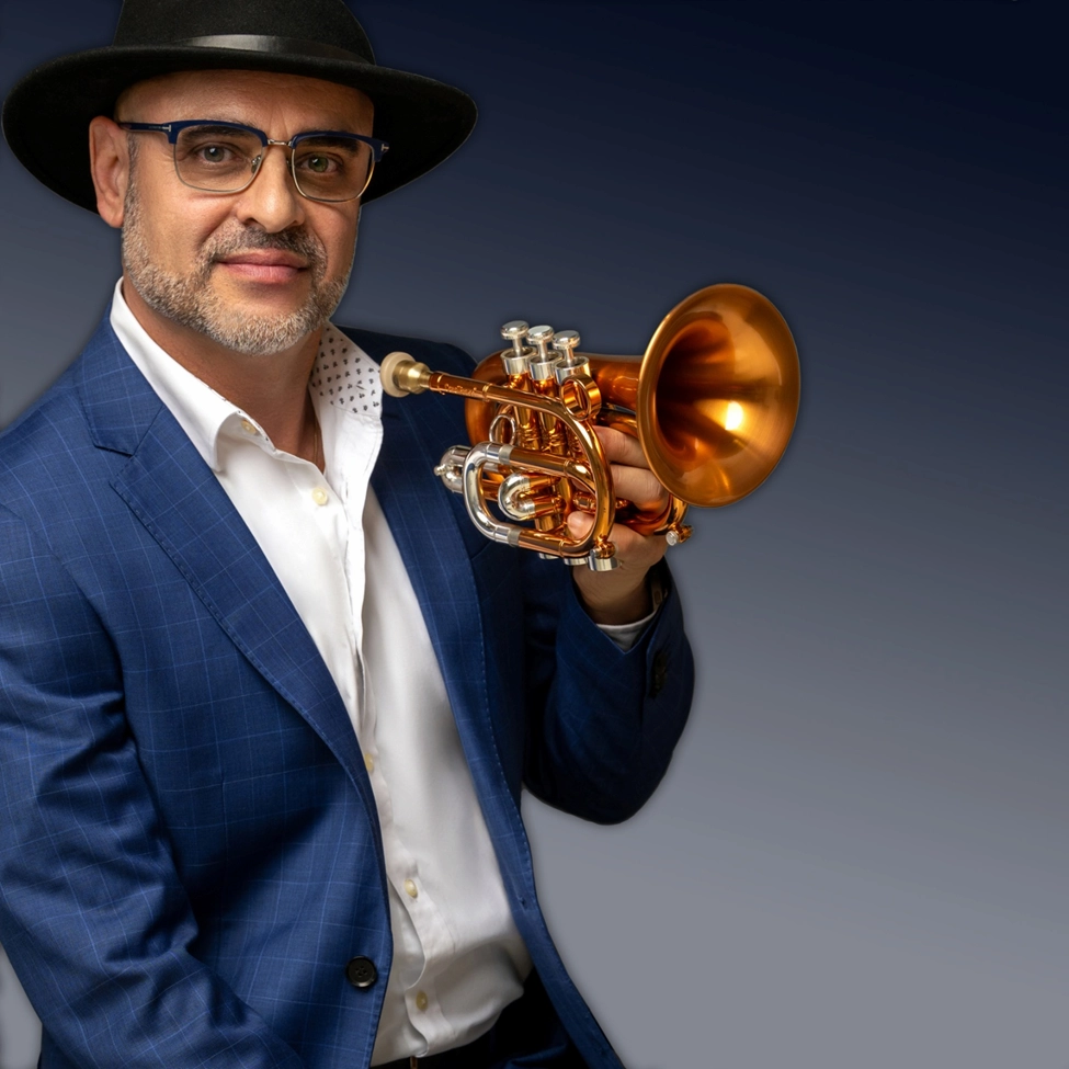 Bill colletti holding a flugelhorn while posing in a blue checkered suit and hat.