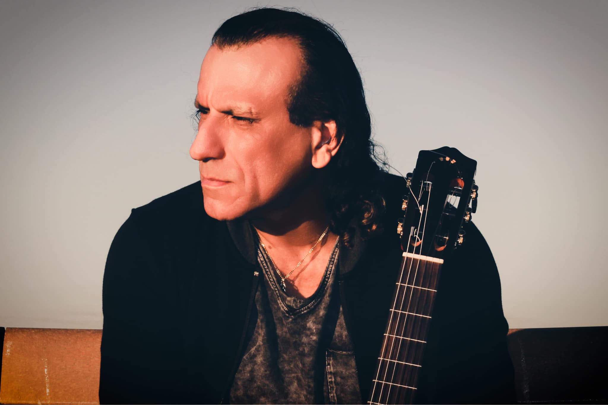 Dorian Ávila seated with a classical guitar, looking to the side against a warm gradient backdrop.