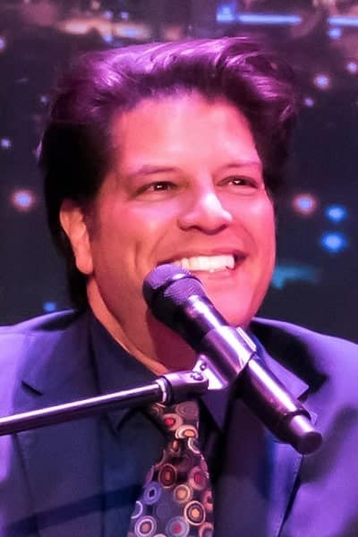 George bugatti singing onstage with a warm smile.