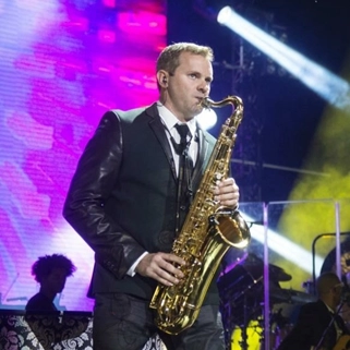 John michalak playing saxophone on a brightly lit stage.