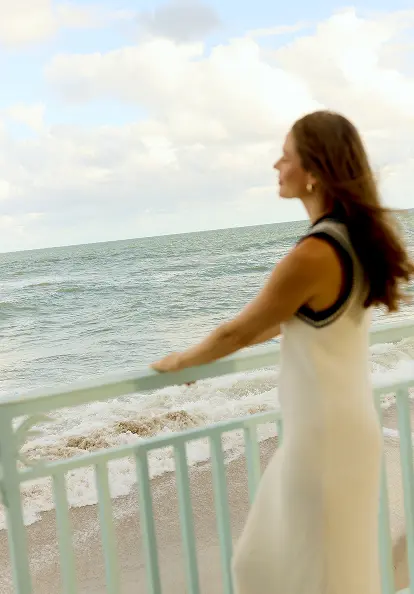 Woman standing on seaside balcony overlooking ocean waves under cloudy sky