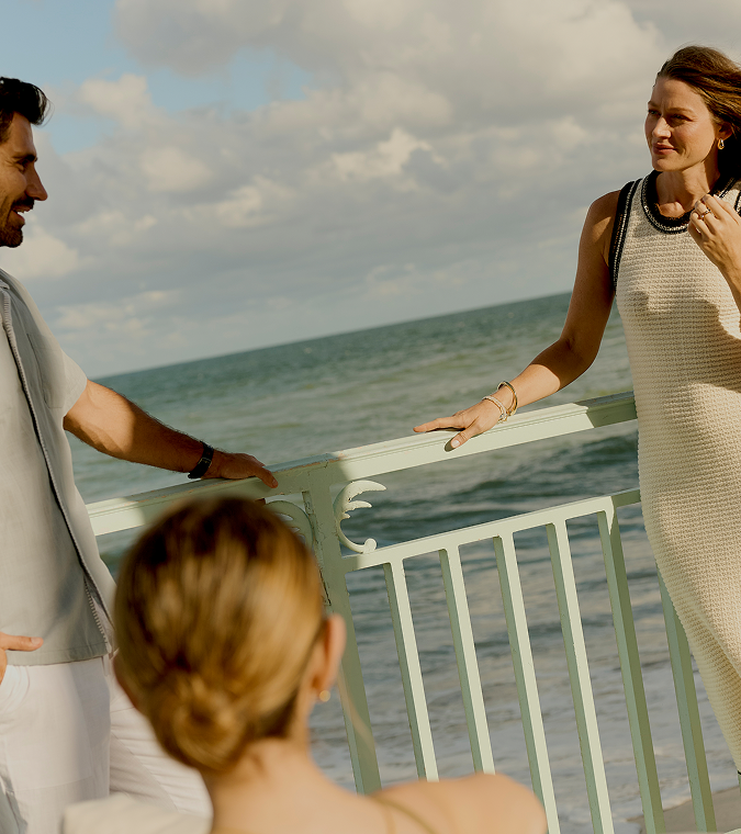 Couple talking on seaside balcony with ocean waves and cloudy sky behind