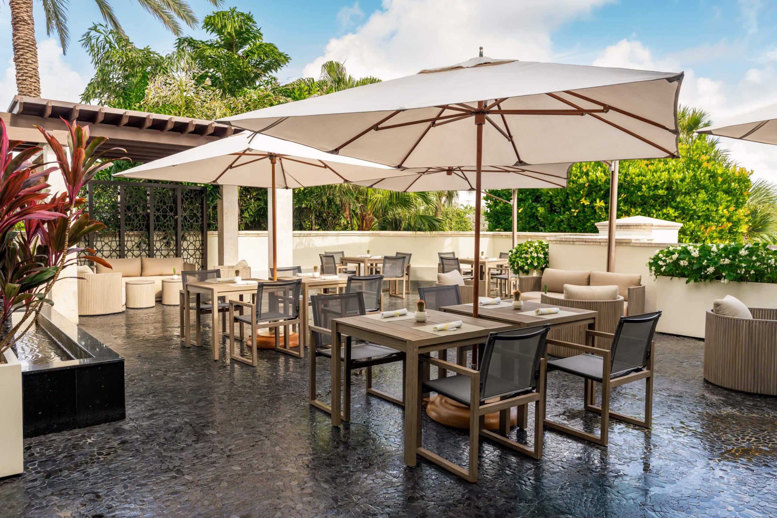 Outdoor patio dining area with umbrellas, wooden tables, and lush tropical greenery