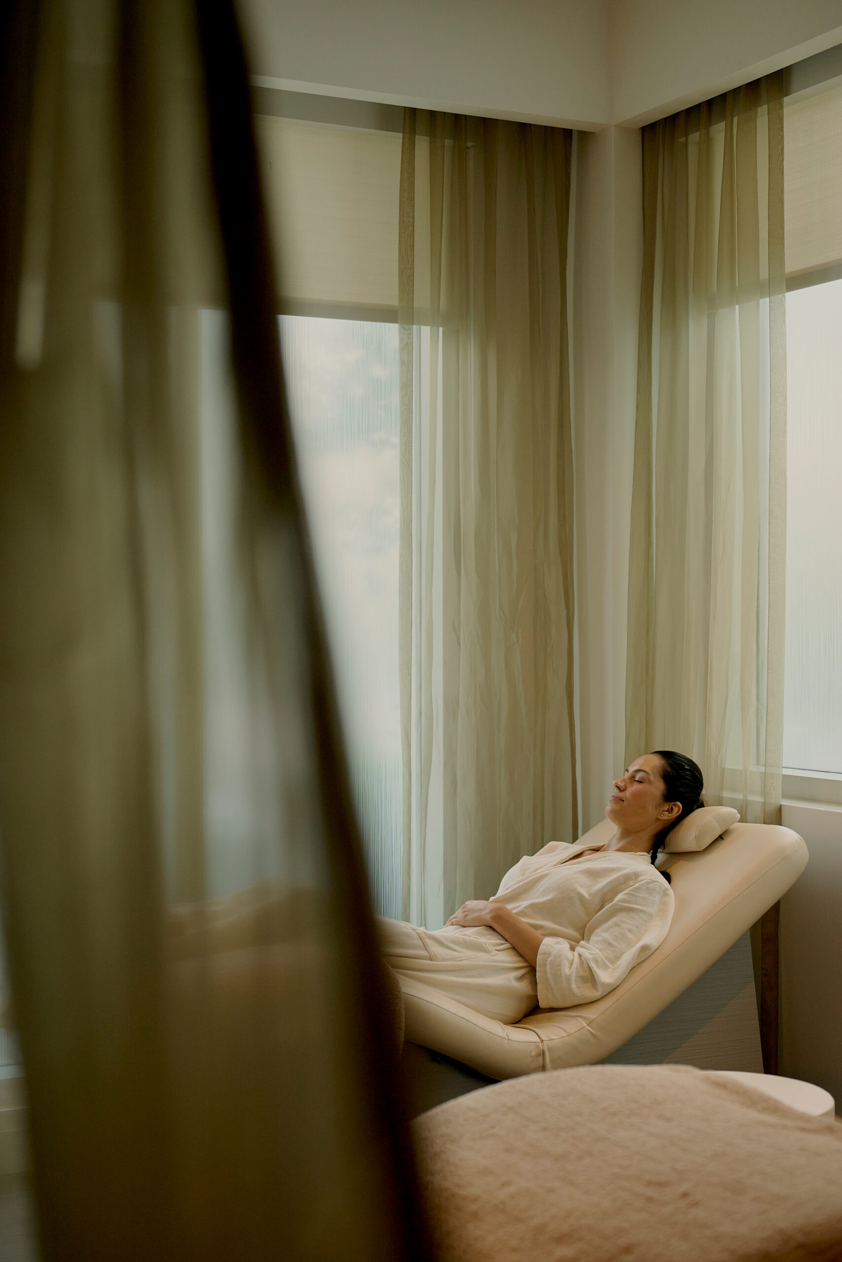 Woman relaxing on lounge chair in serene spa room with soft curtains