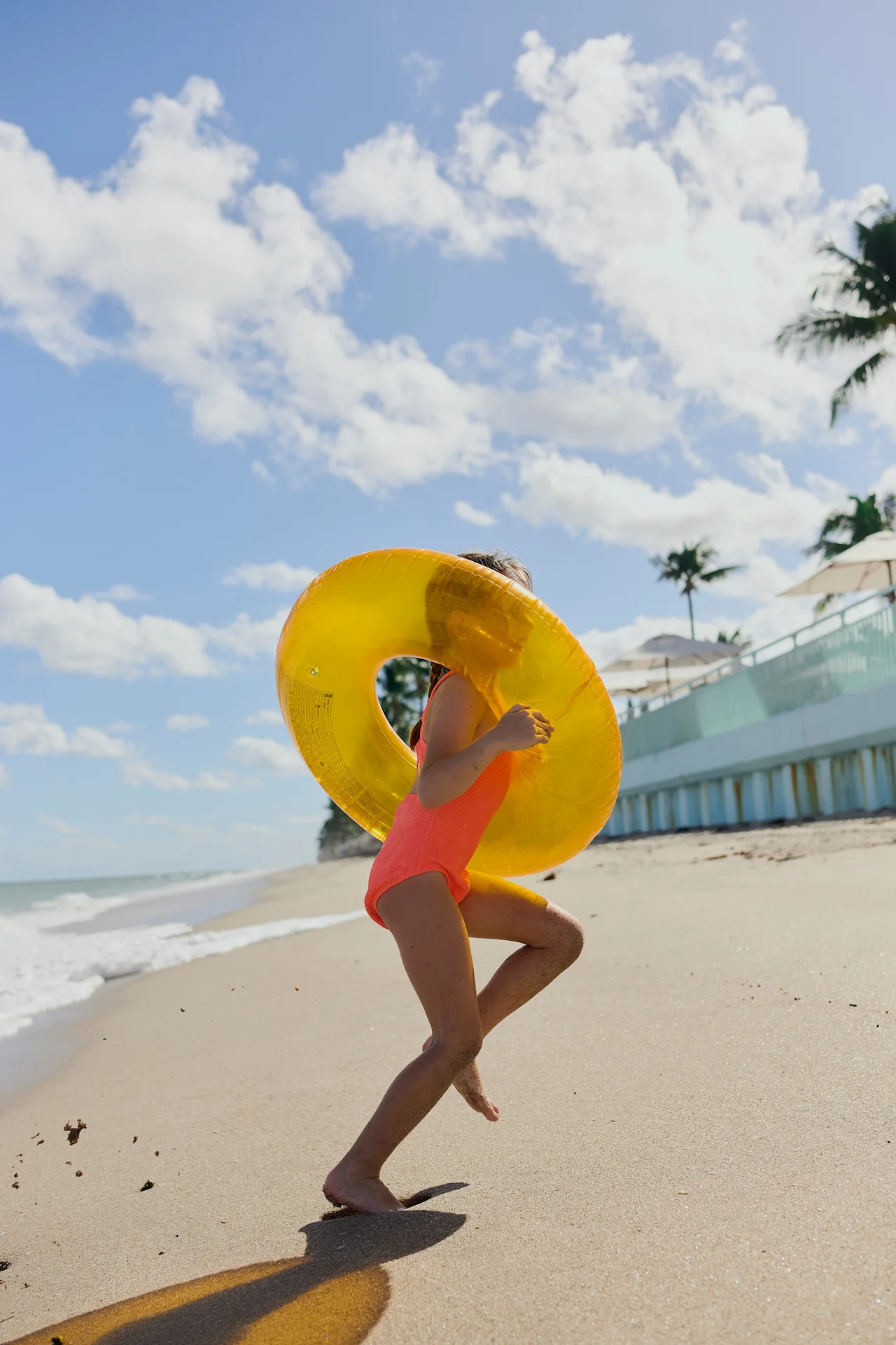 Child running along the sandy beach with a bright yellow float ring on a sunny day by the ocean