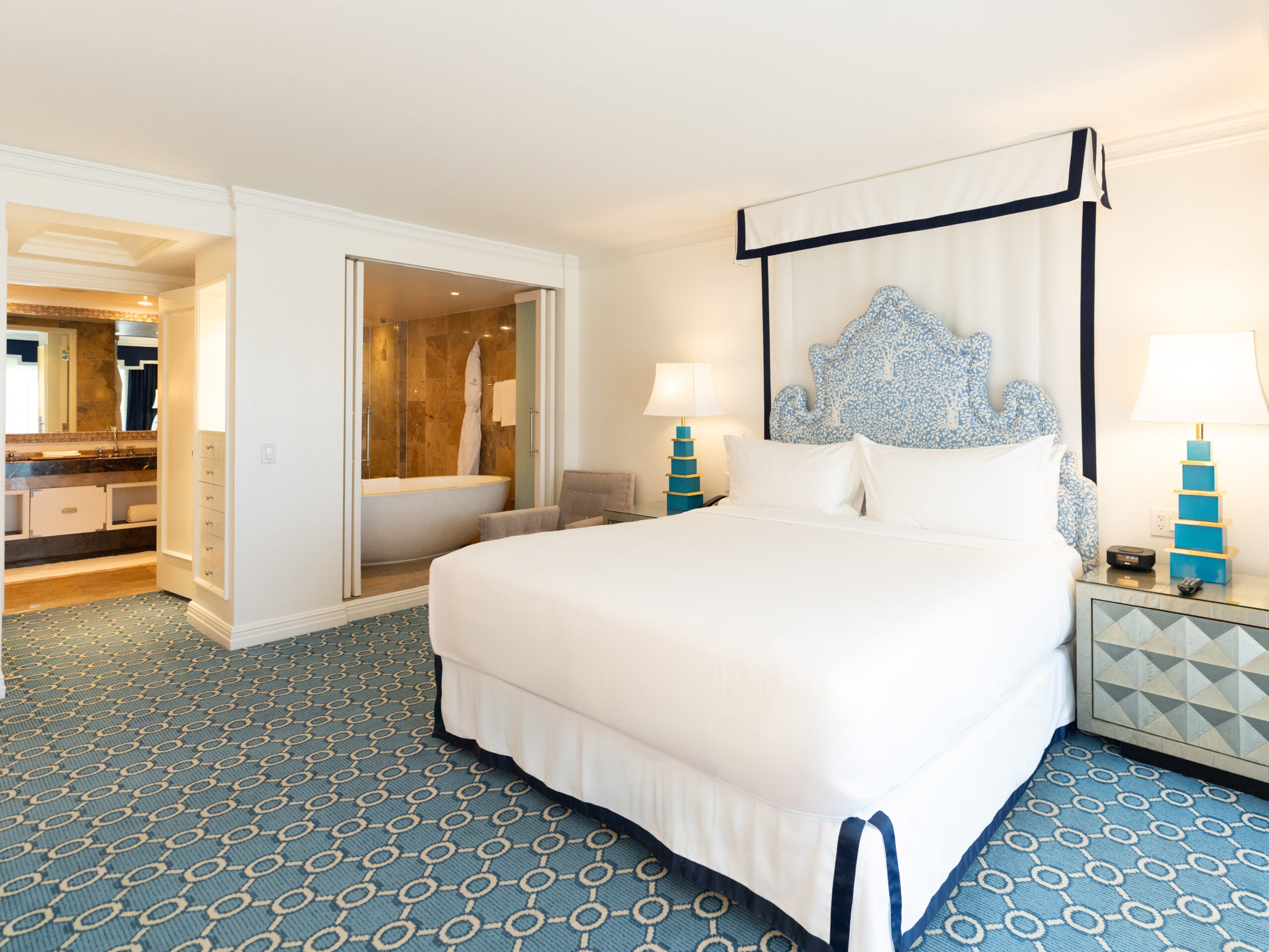 Luxury hotel bedroom with king bed, blue headboard, and open bathroom with soaking tub