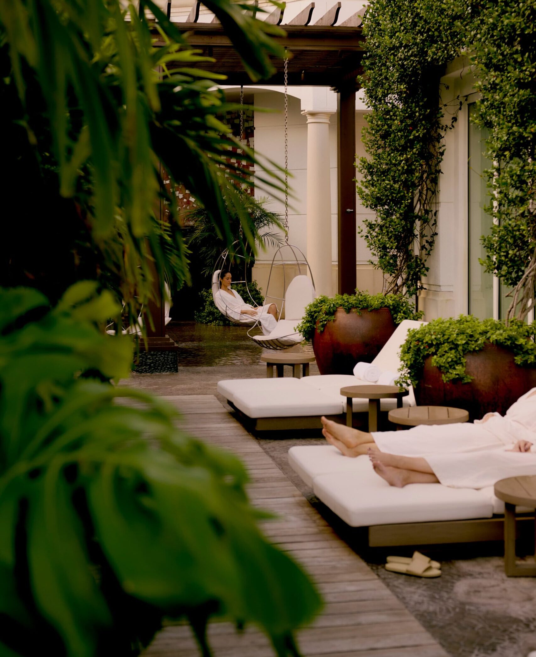 Guests relaxing on loungers and swing chair in lush outdoor spa courtyard
