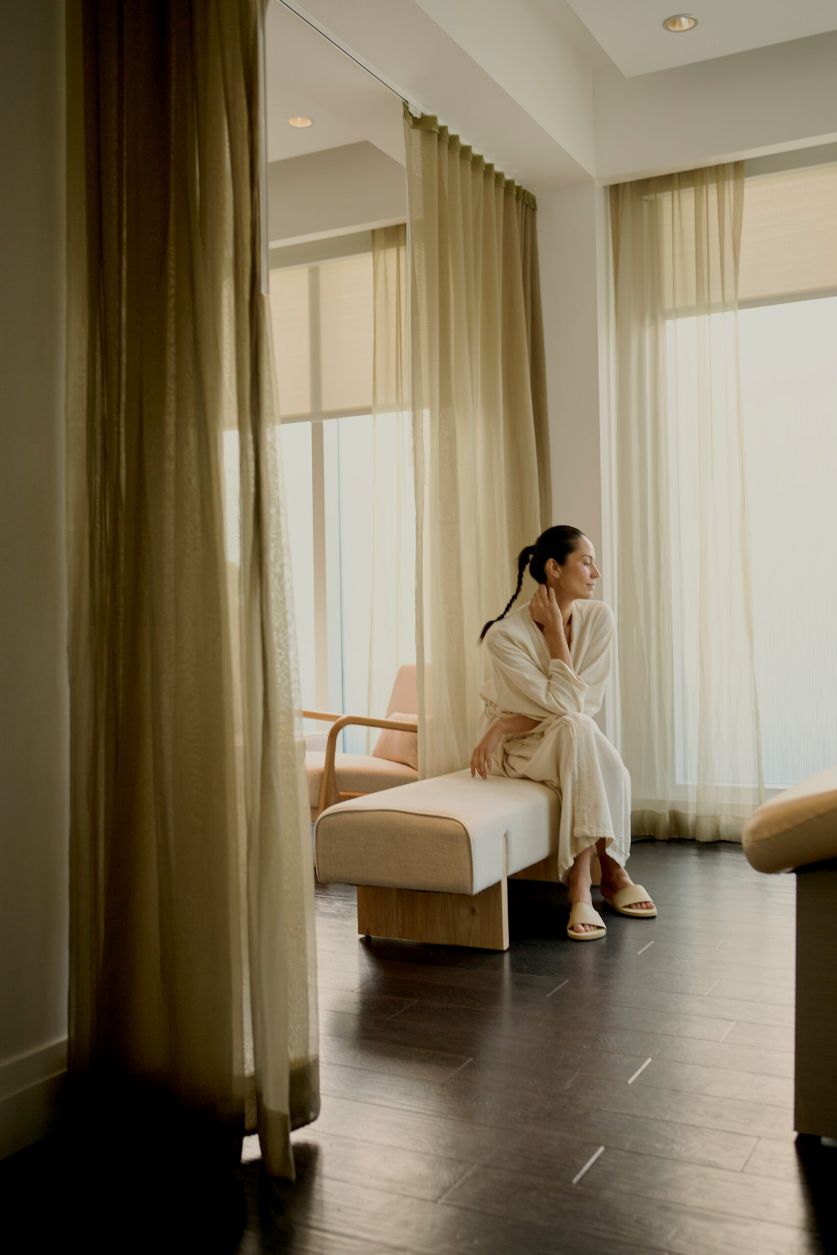 Woman in robe sitting on bench in serene spa room with soft natural light