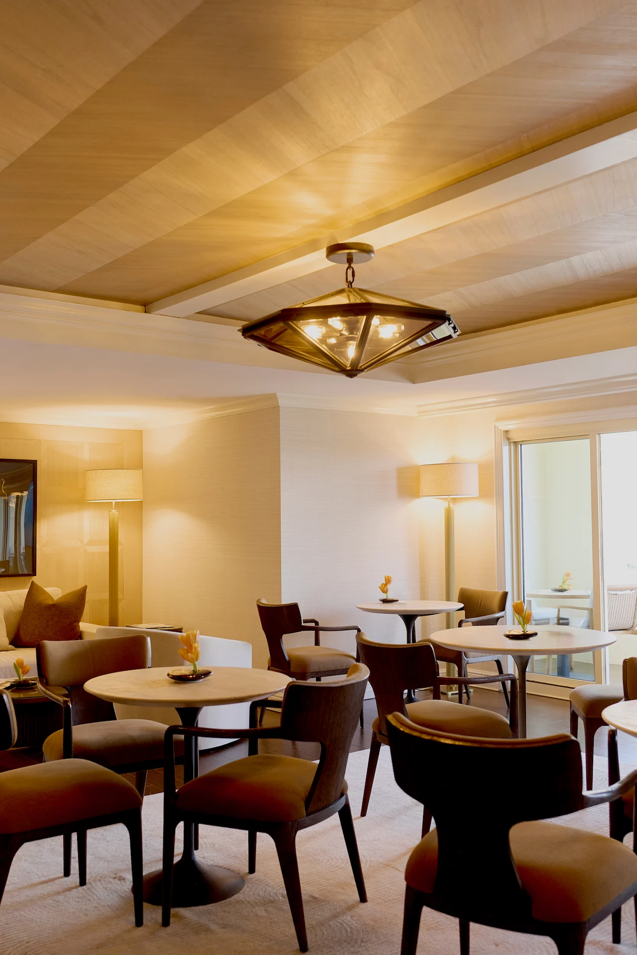Warm, modern room with round tables, dark wood chairs and soft ambient lighting