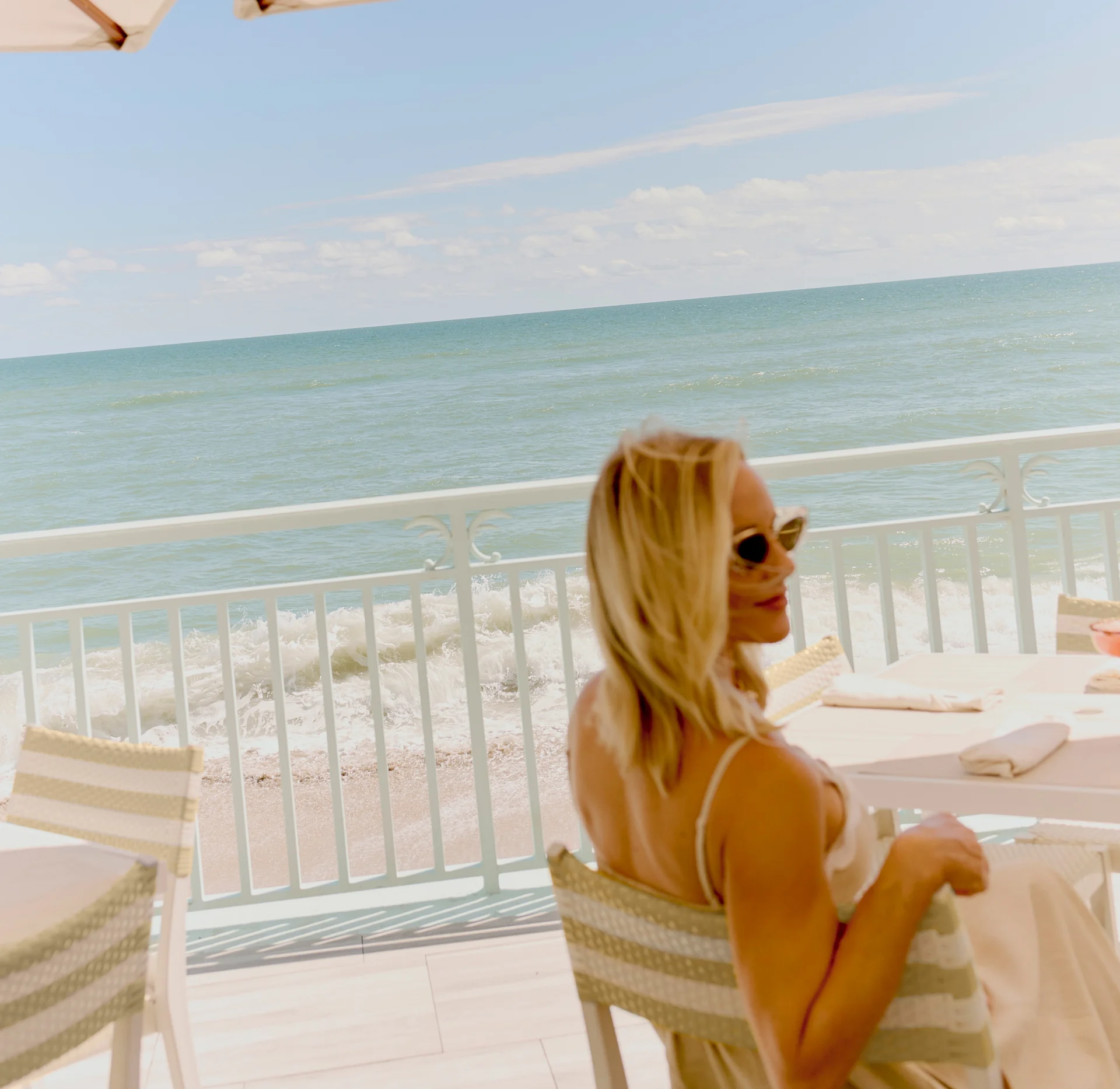 Woman relaxing at breeze ocean kitchen’s shaded oceanfront table with calm waves and soft coastal light