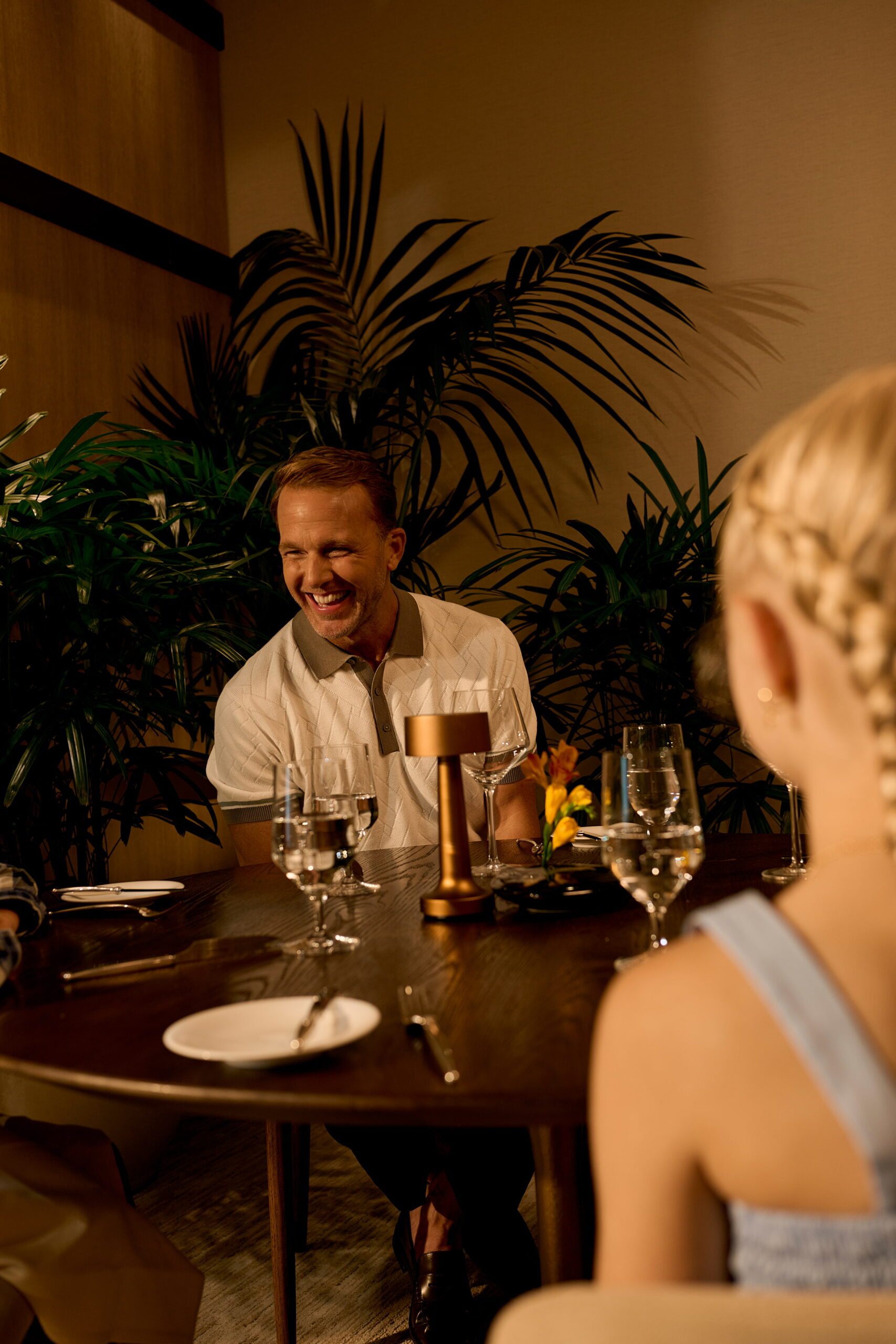 Man smiling at dinner table with guests in warmly lit restaurant setting