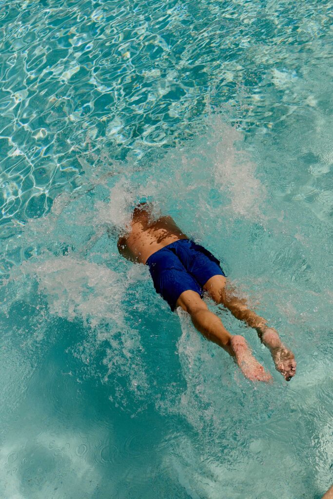Man diving into clear turquoise pool water creating splash and ripples
