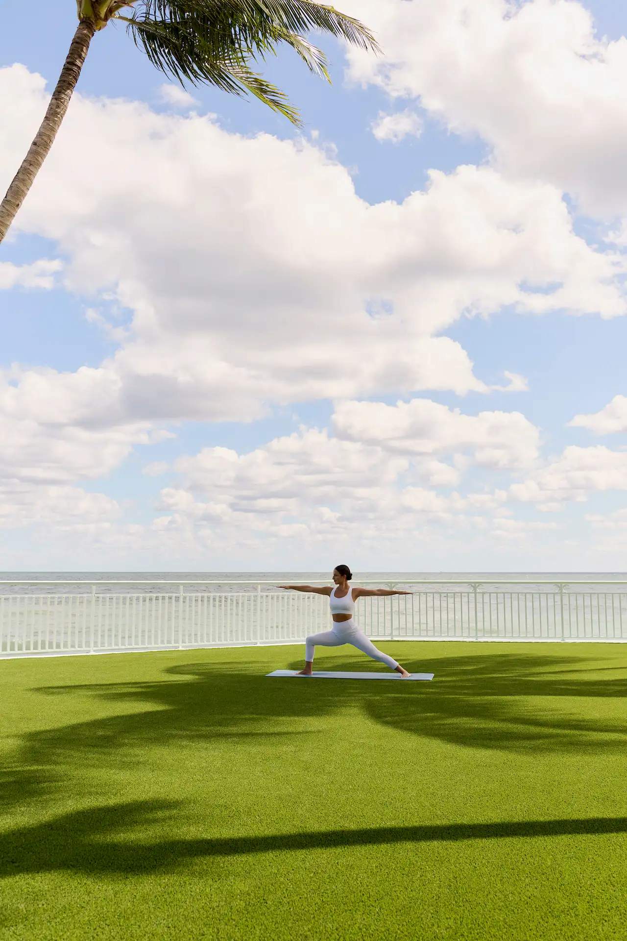 Person doing a warrior ii yoga pose on a lawn with ocean views.