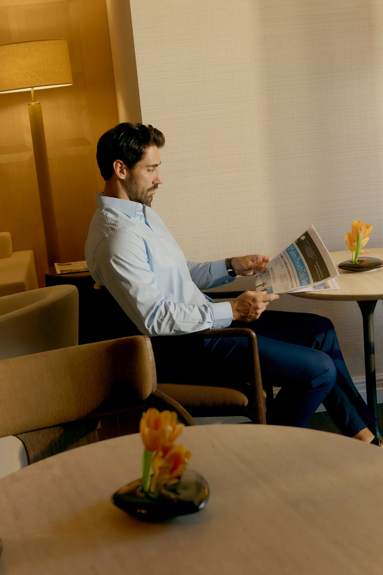 Guest reading a newspaper in a warm lounge with soft lighting and tulips on the table